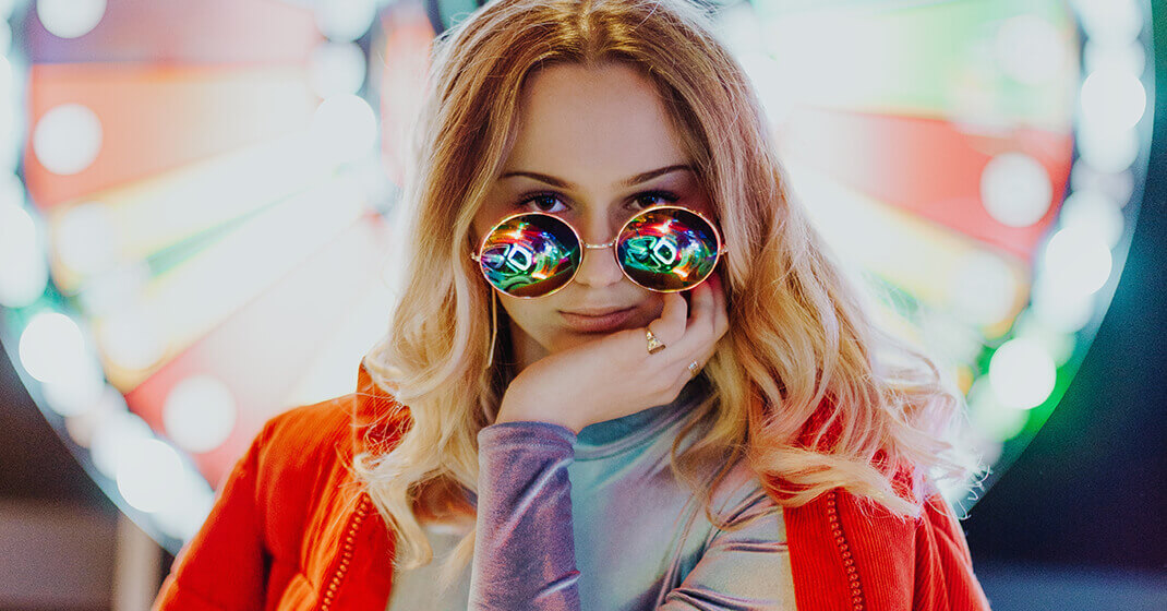 woman in front of ferris wheel lights and wearing rainbow sunglasses