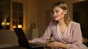 woman smiling at her laptop in a dim lit room